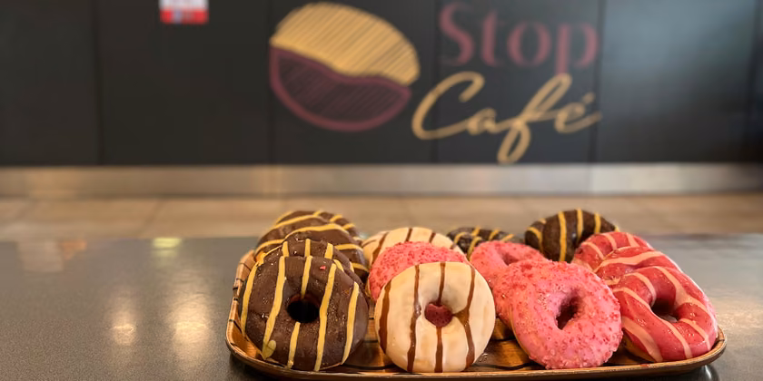 Bandeja de donuts glaseados sobre el mesón, bajo el letrero de Stop Café.